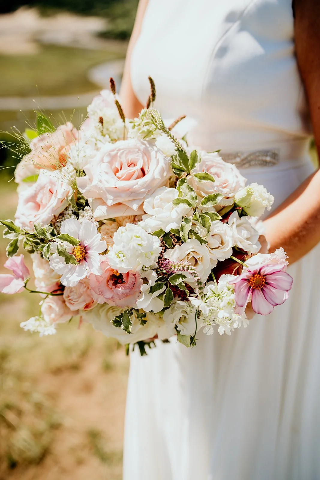 Bridal bouquet with pink and white flowers being held by a bride in a simple white wedding dress. 