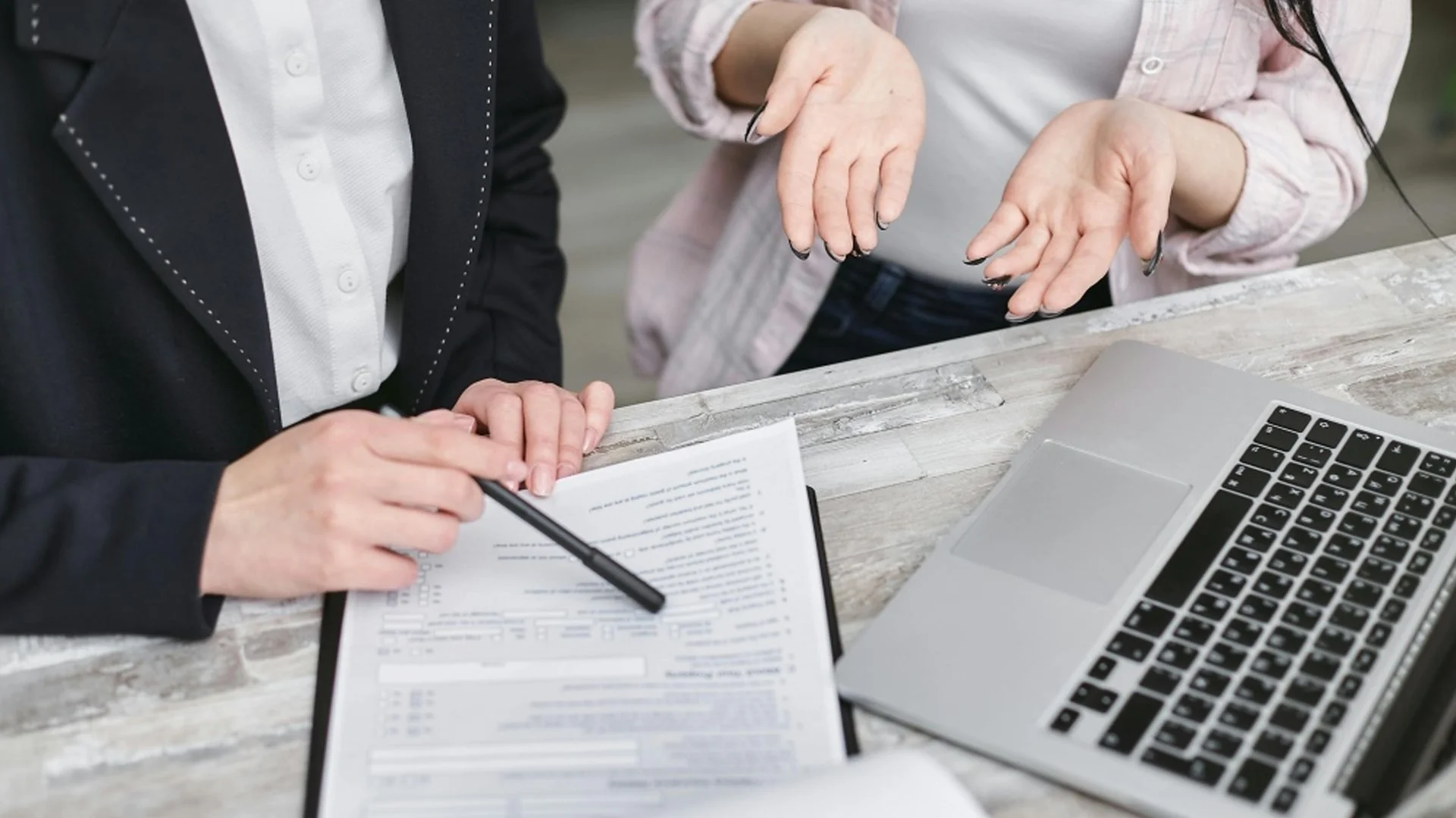 Deux personnes discutent à une table avec un ordinateur portable et un formulaire.