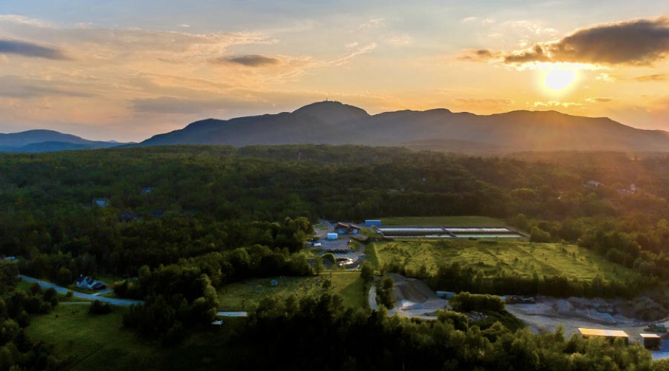 Paysage rural avec montagnes, forêt, bâtiments agricoles et champs au coucher du soleil.