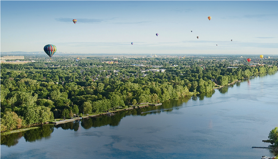 De nombreux ballons à air chaud flottent au-dessus d'une rivière bordée d'arbres.
