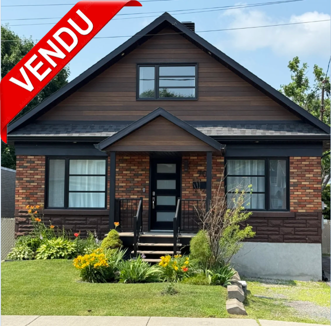 Maison en pierre avec un balcon, devant un jardin avec fleurs et arbustes, indication VENDU en haut à gauche