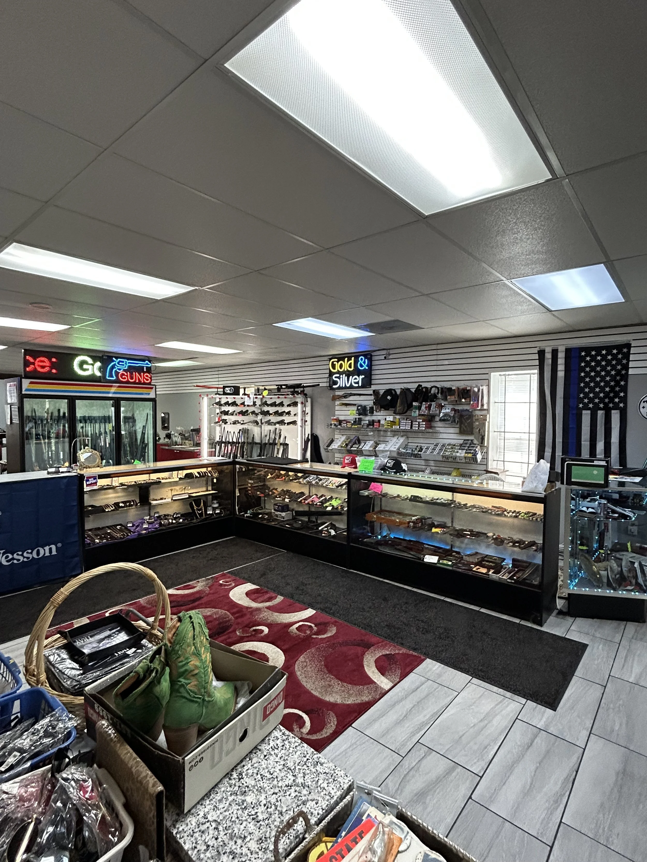 An interior view of a store selling guns, ammunition, and related accessories, with display cases, signs, and American flag.