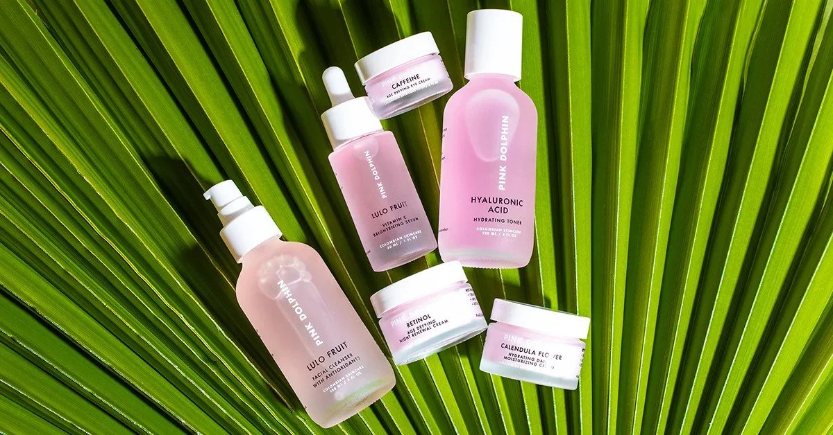 Skincare products with pink labels placed on a large green palm leaf