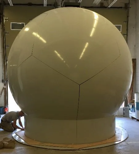 A large spherical structure inside a workshop, with a person working nearby.