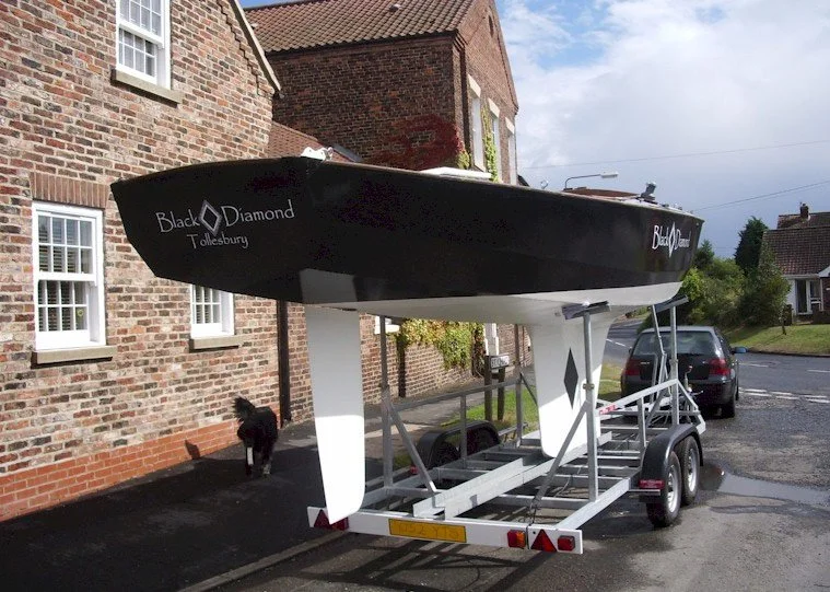 A small black boat on a trailer parked next to a brick house on a residential street