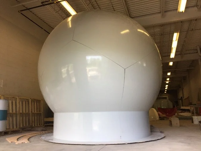 A large white spherical structure with panel lines inside an industrial warehouse.