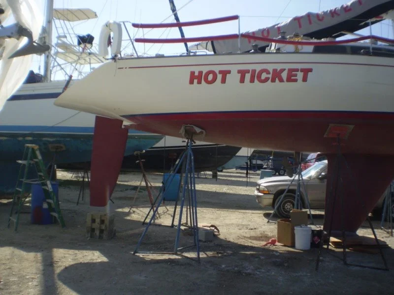 A boat named "Hot Ticket" on land in a boatyard, with tools and a car nearby.
