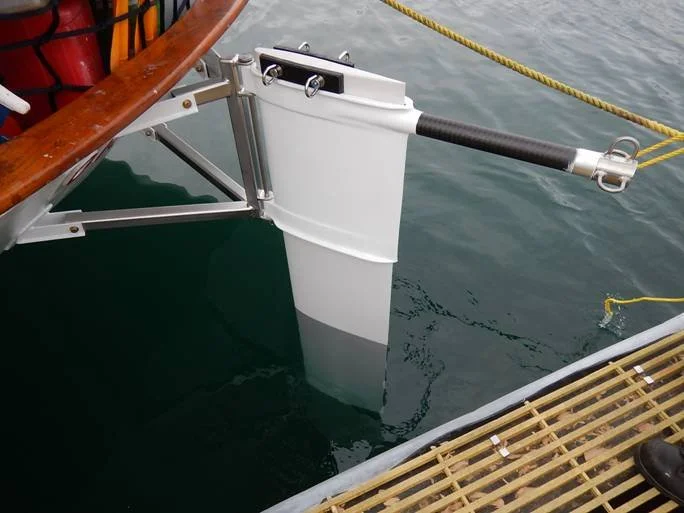 Close-up of a boat's hull and bow, with a white propeller and a hydraulic lifting mechanism, docked beside a wooden pier, with a yellow rope tied to the boat.
