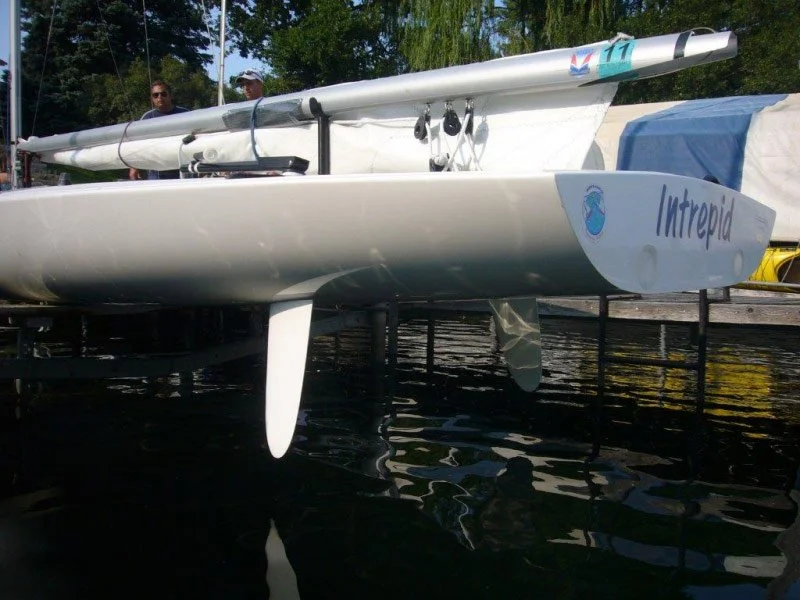 A sailboat docked on the water with the name "Intrepid" on its stern and a logo of a blue whale. The boat has a sail with the number 11 and is resting on a black support structure.