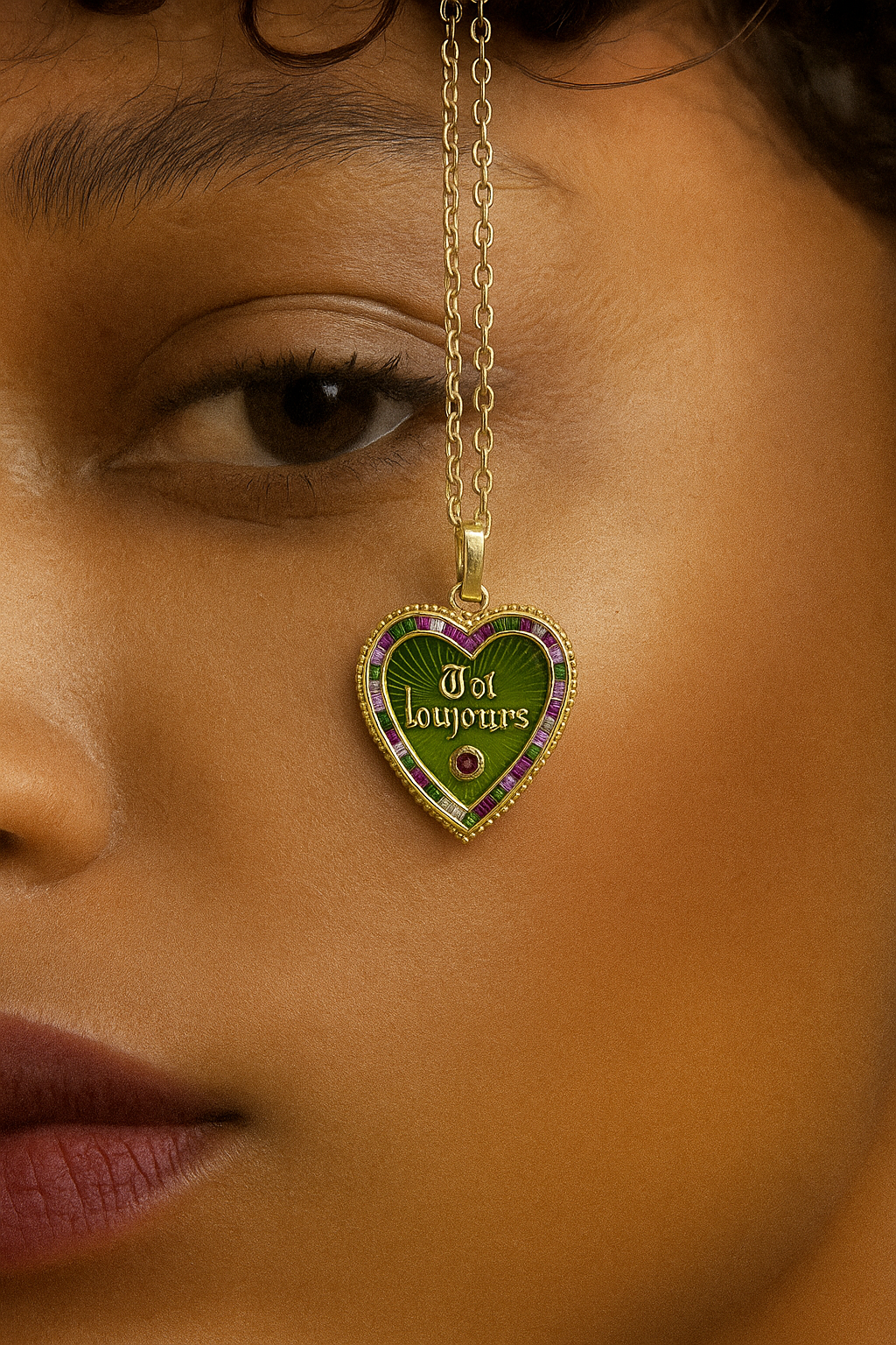 Un collier avec un pendentif en forme de cœur, portant l'inscription 'Toi Toujours', suspendu devant le visage d'une personne. La personne a la peau claire, des lèvres légèrement mordues, et un œil visible, avec des sourcils fins et des cheveux foncés.