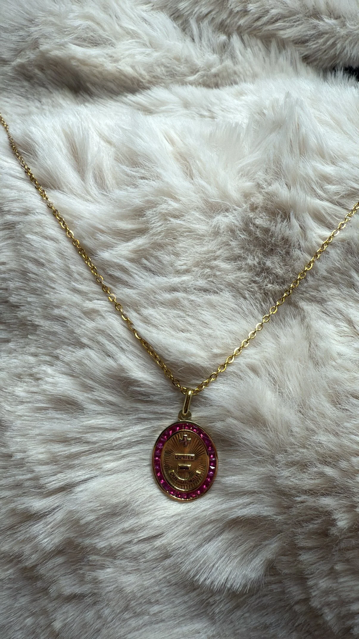 Chaîne en or avec un pendentif oval en or rose entouré de pierres roses, posé sur une fourrure blanche