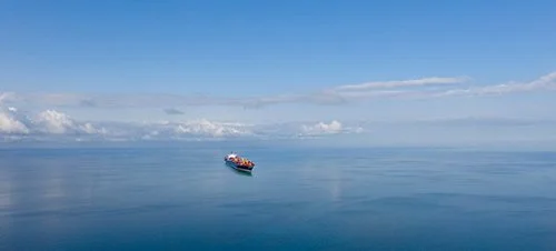 Large cargo ship sailing on calm ocean waters with a partly cloudy sky above.