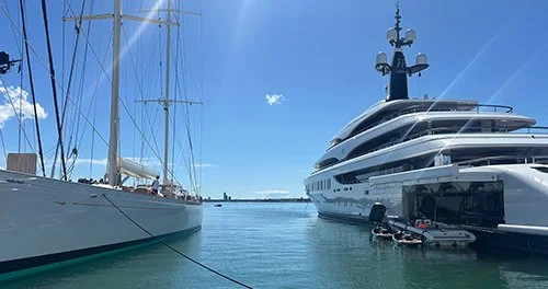 View of a marina with sailboats and a large luxury yacht docked, clear blue sky, and calm water.