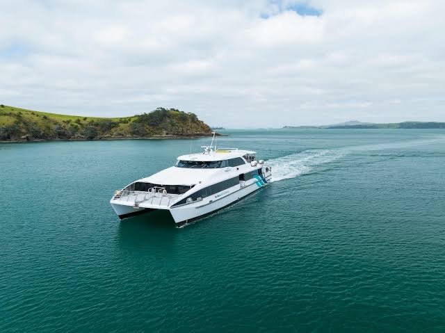Fullers Ferry cruising on calm turquoise water near a green hilly coastline.