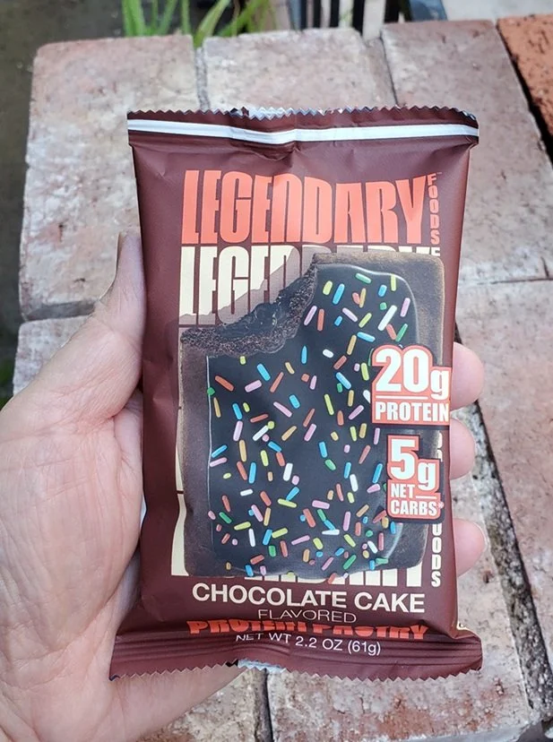 A hand holding a packaged Legendary Chocolate Cake flavored protein pastry,
