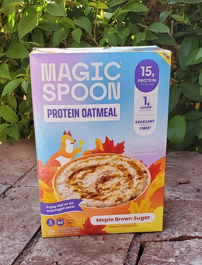 Box of Magic Spoon Maple Brown Sugar Protein Oatmeal displayed outdoors.The package highlights 15g of protein and 1g of sugar per serving