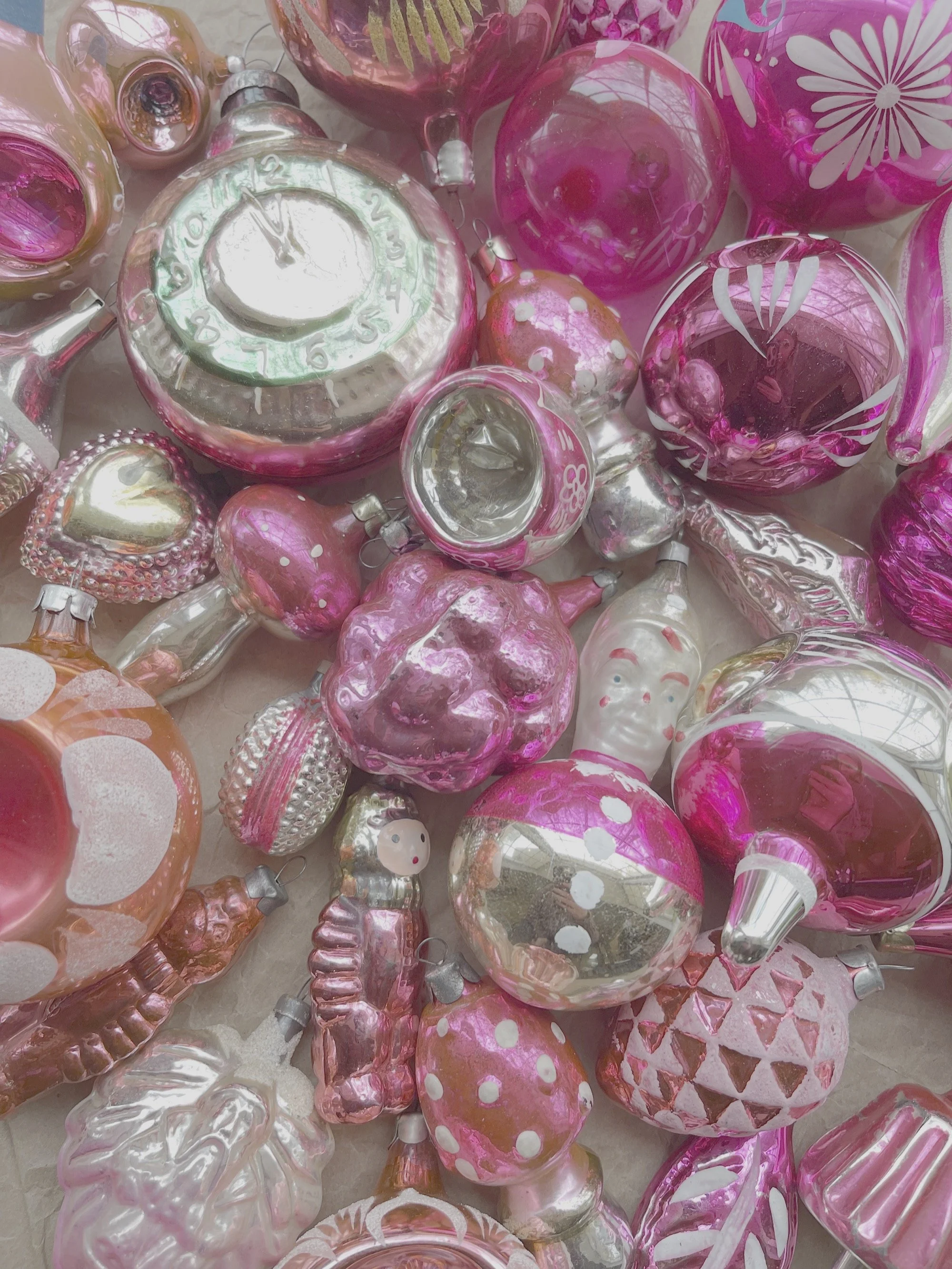 A collection of pink and silver vintage glass Christmas ornaments of various shapes and designs.