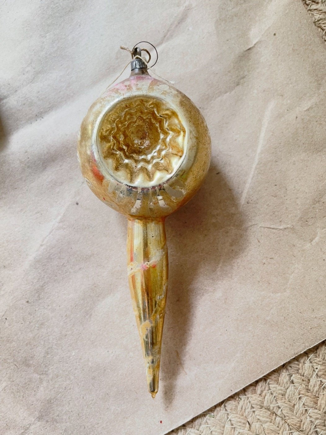 Gold vintage indent Christmas ornament with a pointed teardrop shape on kraft paper