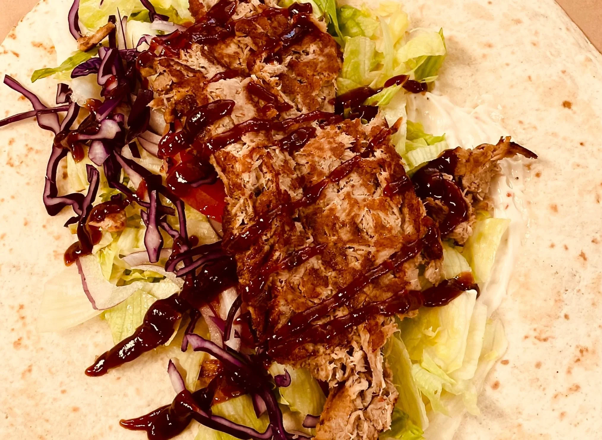 Open taco with shredded lettuce, tomato, chopped onion, shredded pork, and drizzled with barbecue sauce.