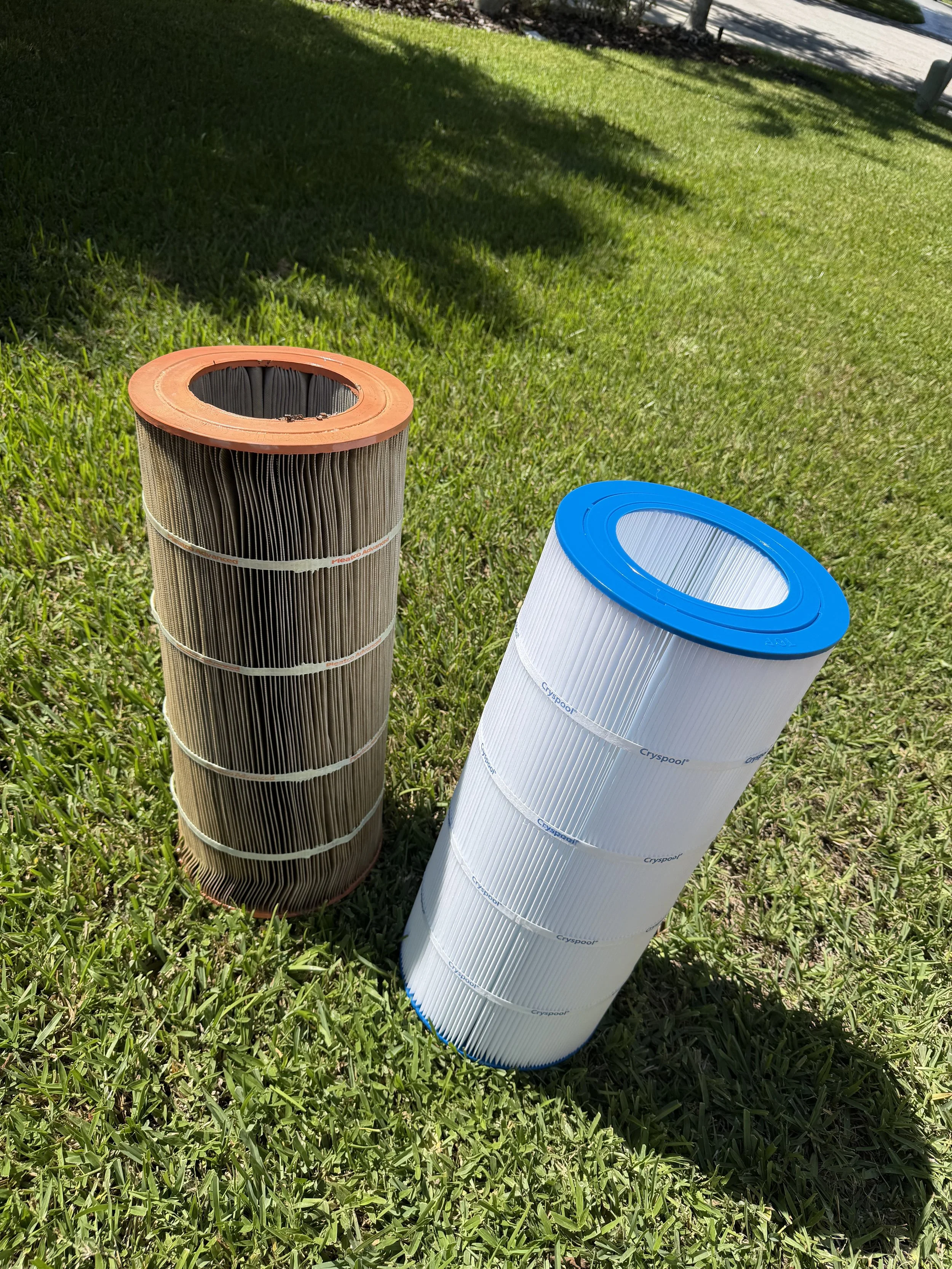 Two pool filters, one dirty and one clean, standing side by side on a pool deck overlooking a swimming pool.