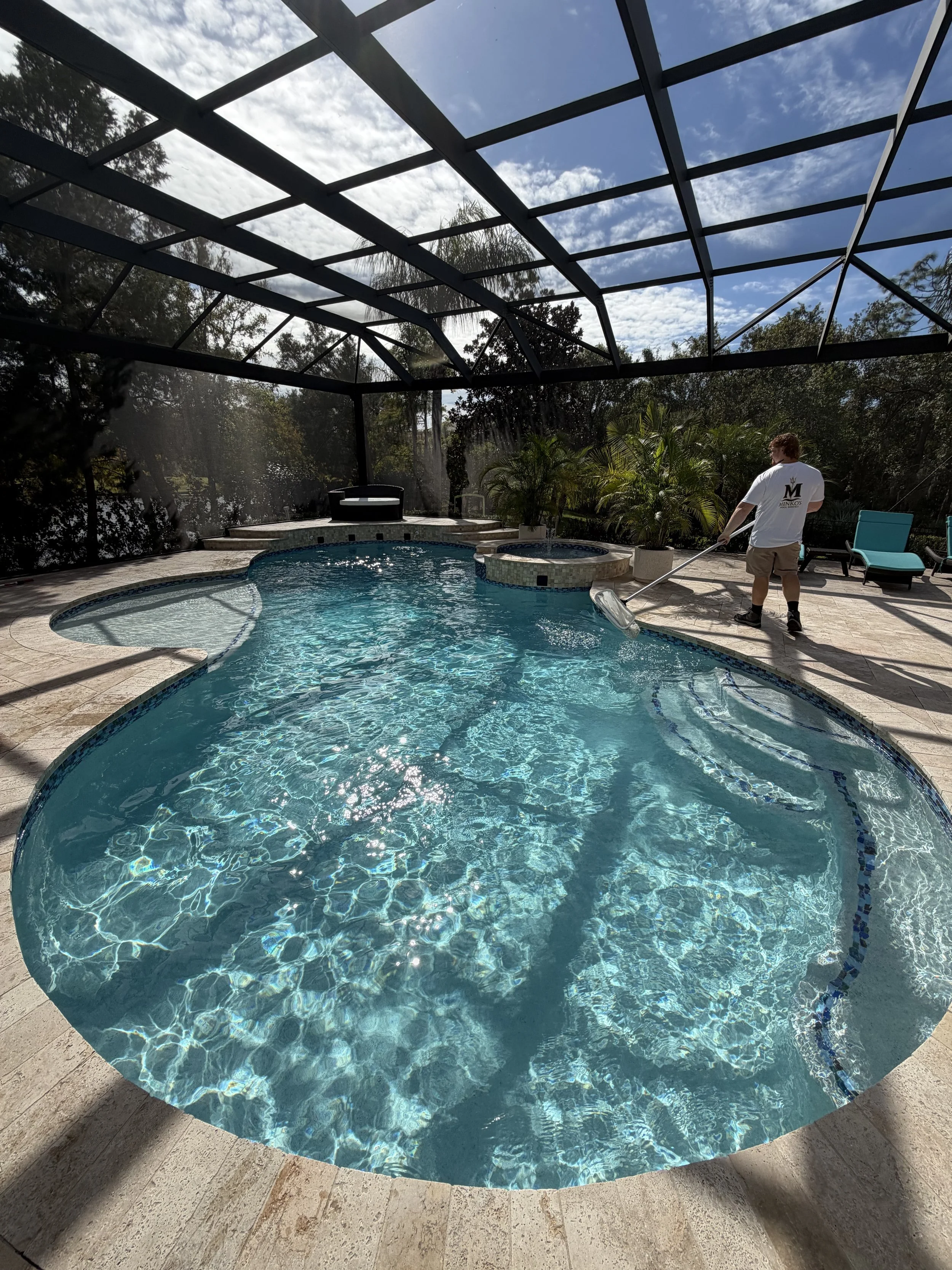 Person with a straw sunhat sitting poolside with legs extended into the pool, viewed from above.