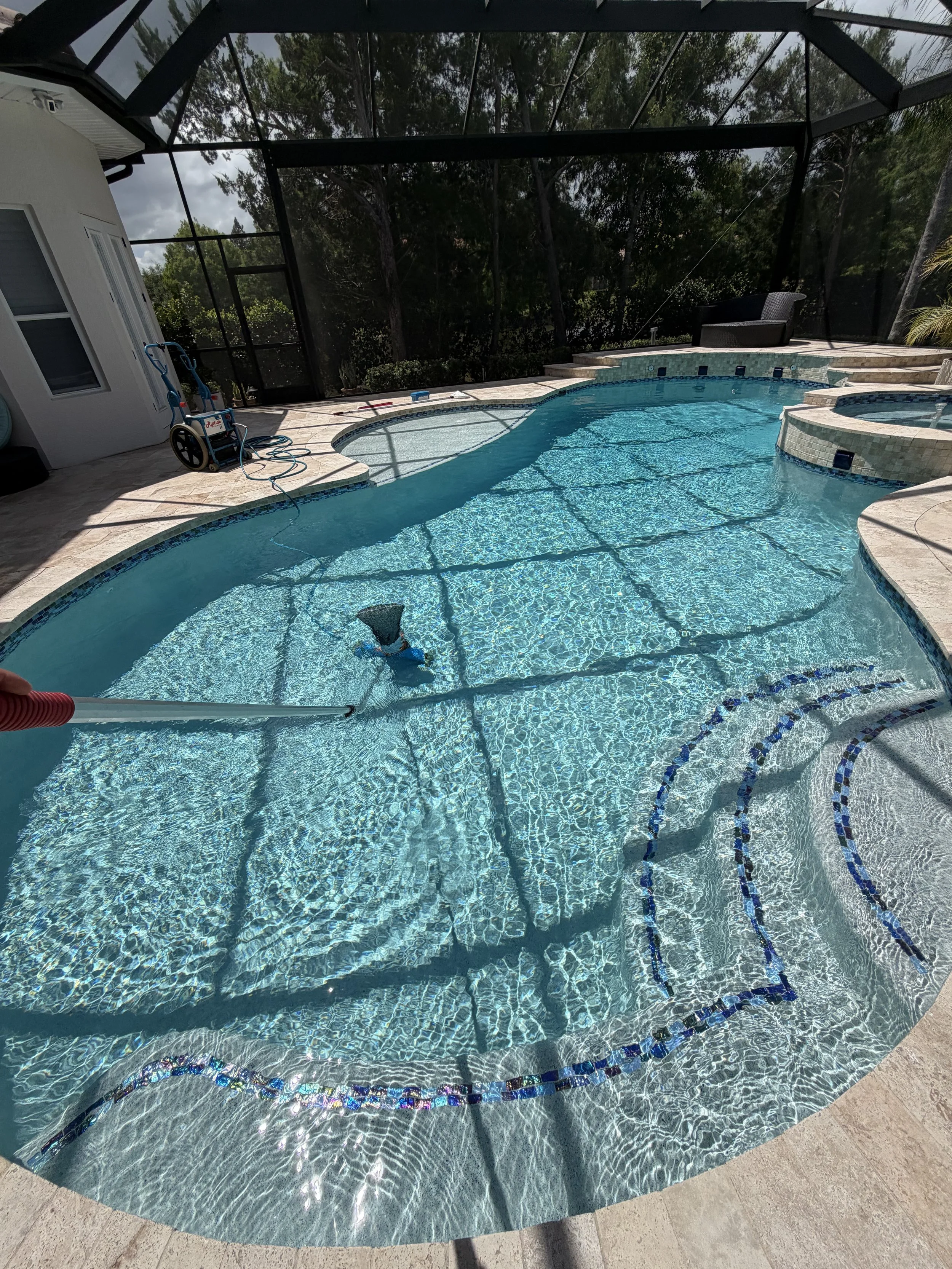 Empty hot tub with a brown brick border, green water, and a pool or another water feature in the background.