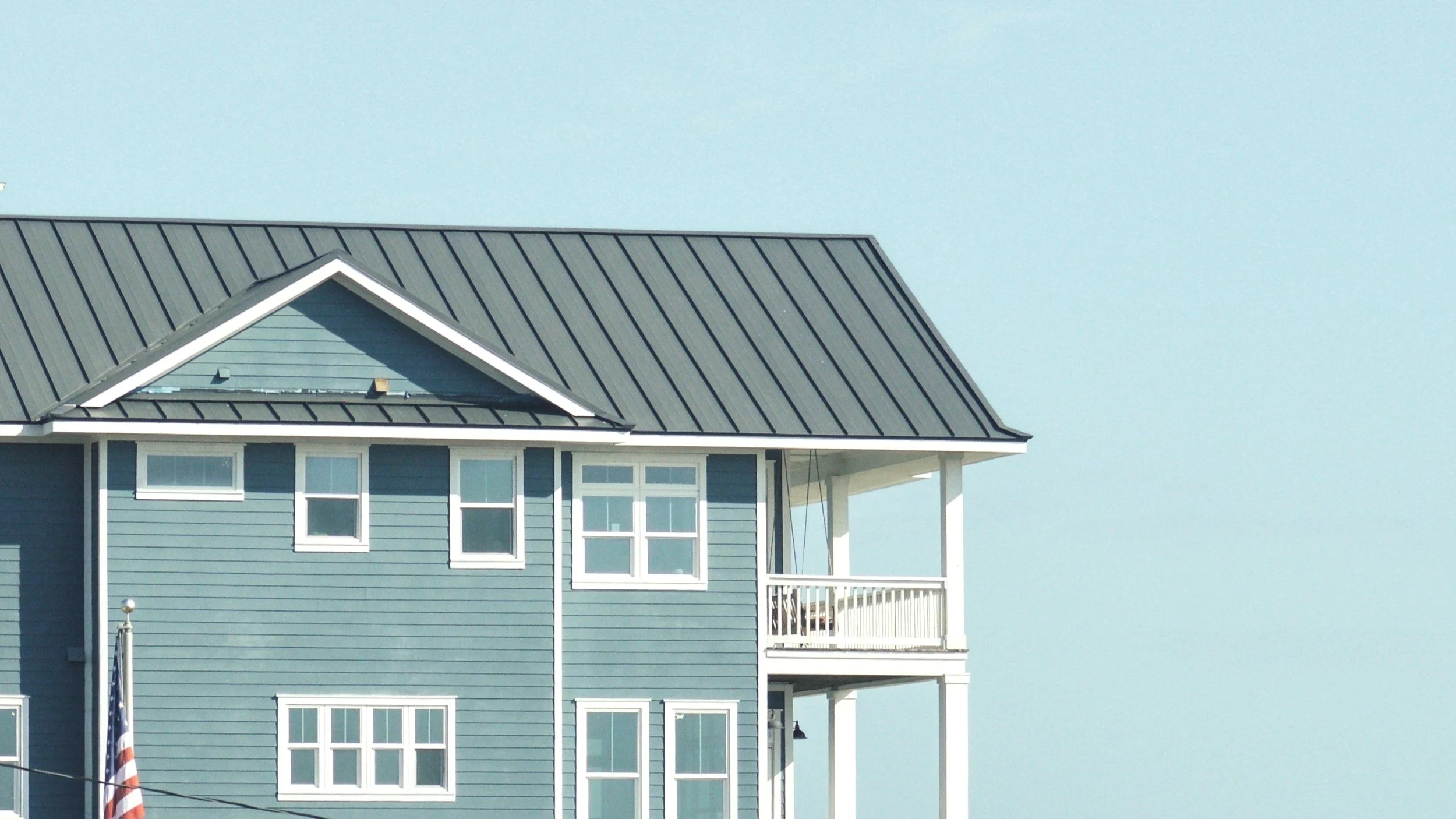 The image depicts the upper part of a blue house with multiple windows and a small balcony, set against a clear sky.