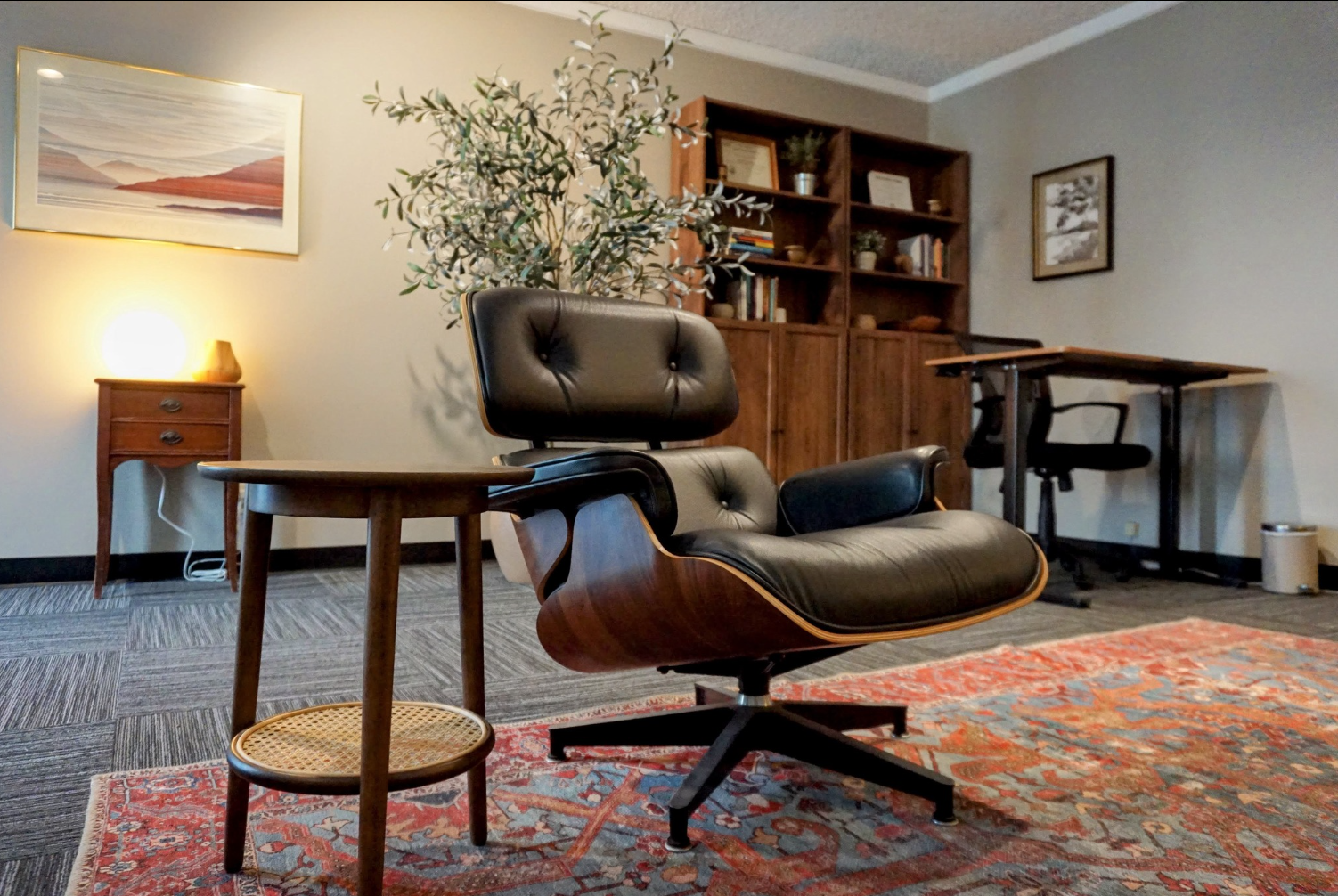 Cozy therapy office in Eagle Rock with a leather lounge chair, side table, bookshelf, desk, framed artwork, plants, and a warm patterned rug.