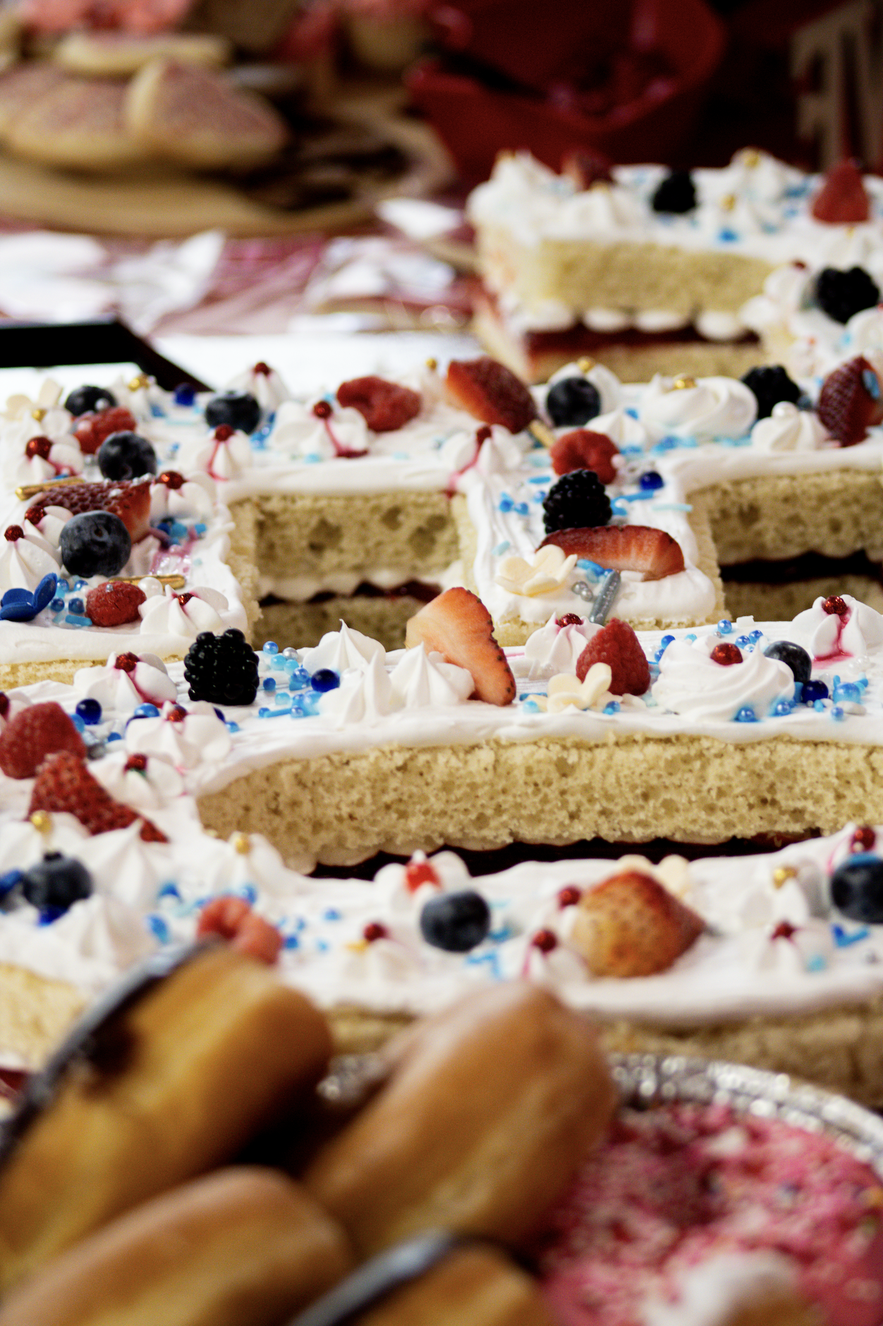 Decorative cake with white icing topped with strawberries, blackberries, blueberries, and sprinkles on a table.