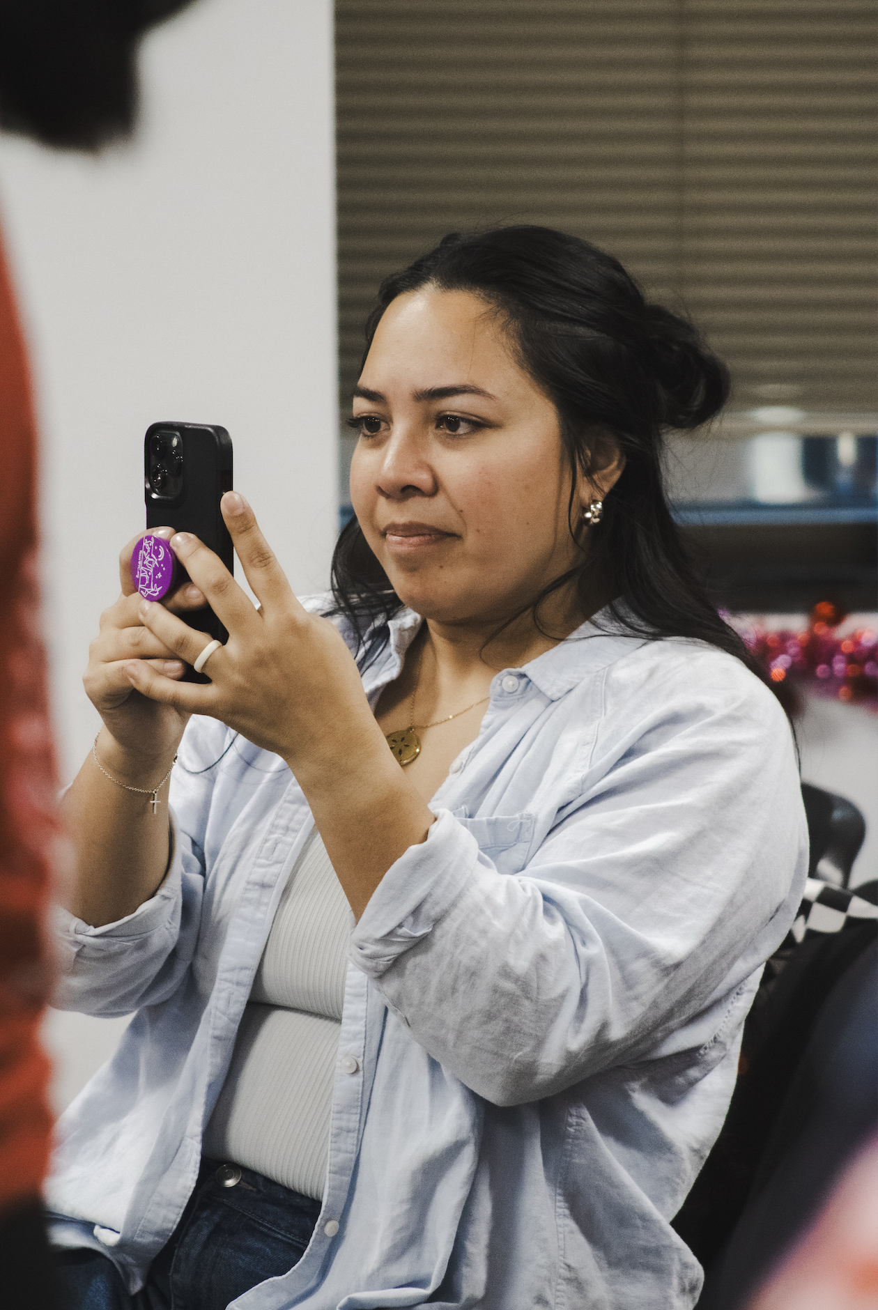 Woman with dark hair and earrings looking at her phone during a celebration or gathering.