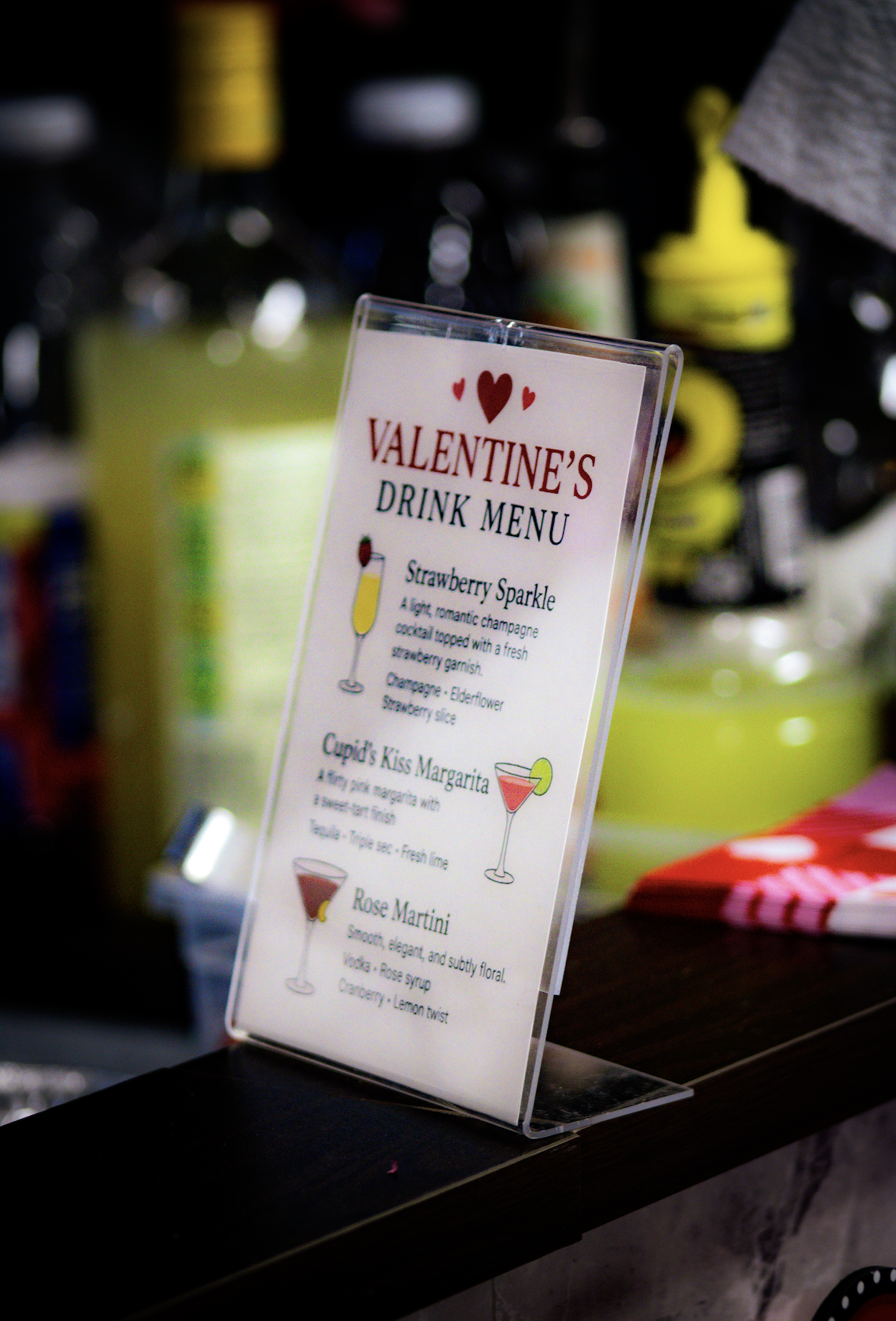 Valentine's Day drink menu with three cocktail options: Strawberry Sparkle, Cupid's Kiss Margarita, and Rose Martini, featuring descriptions and colorful illustrations of each drink.