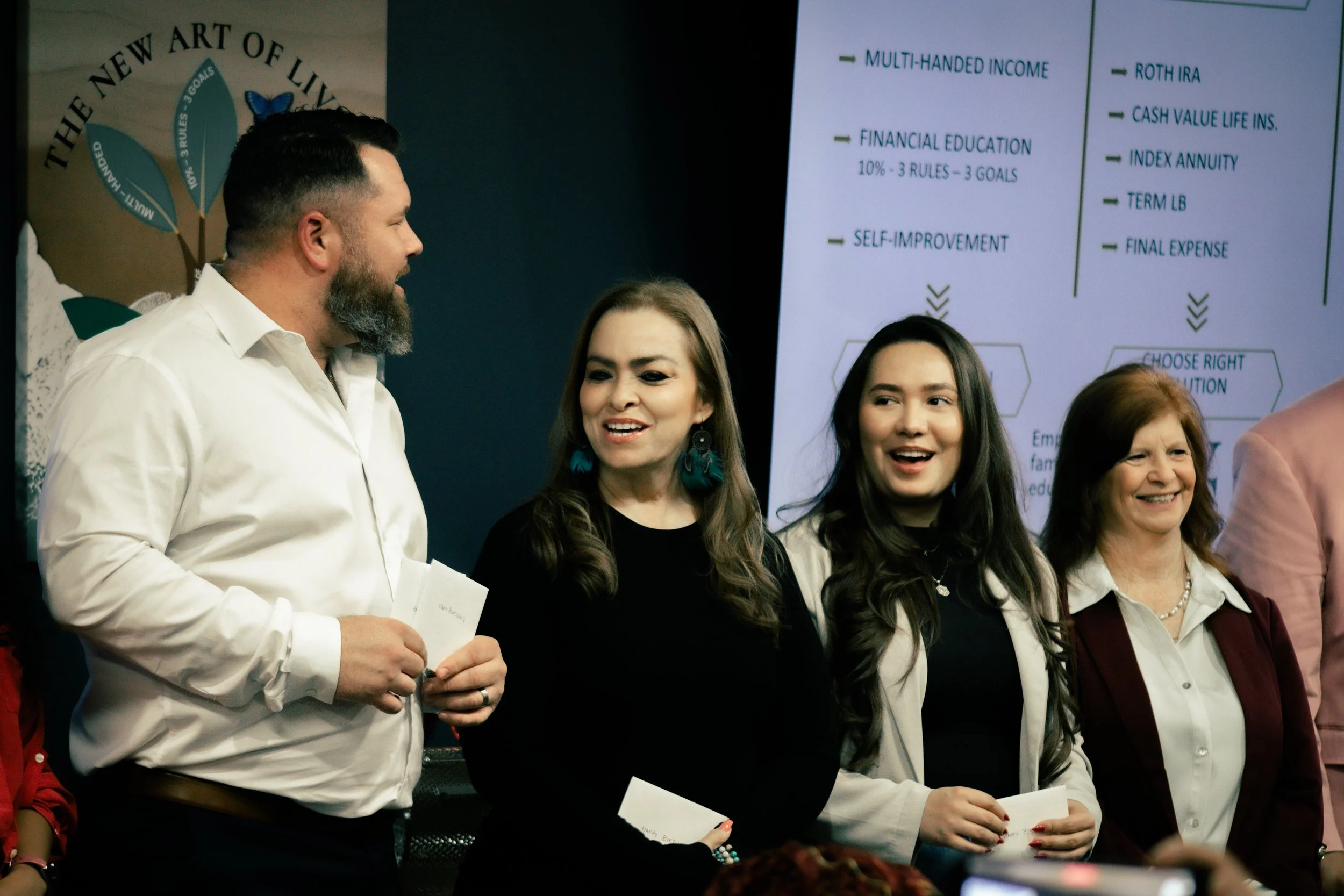 A group of four people, three women and one man, standing in front of a presentation board, engaged in conversation and smiling.