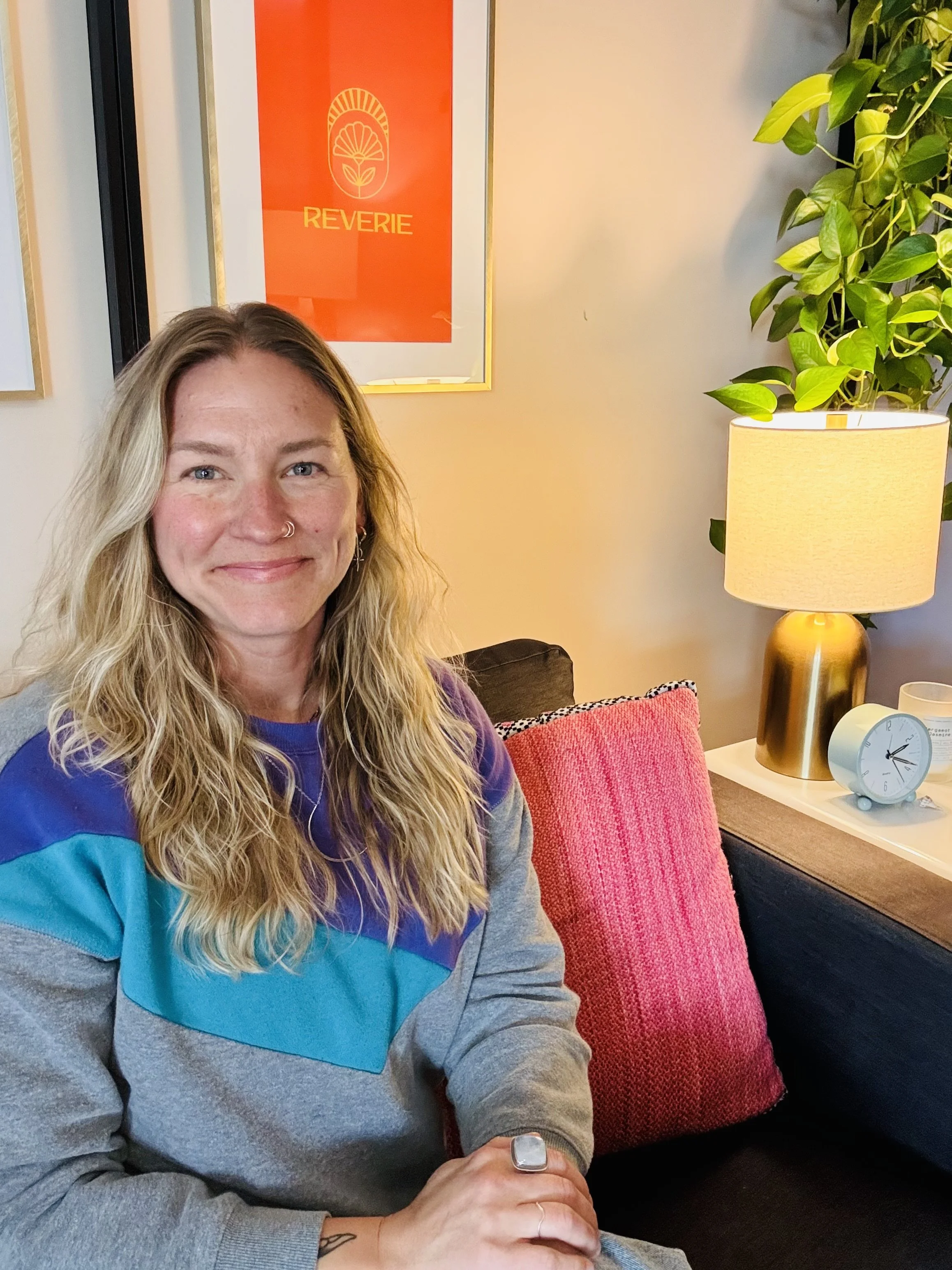 therapist smiling with midcentury modern clock and lamp with pink pillows located in her RiNo therapy safe space