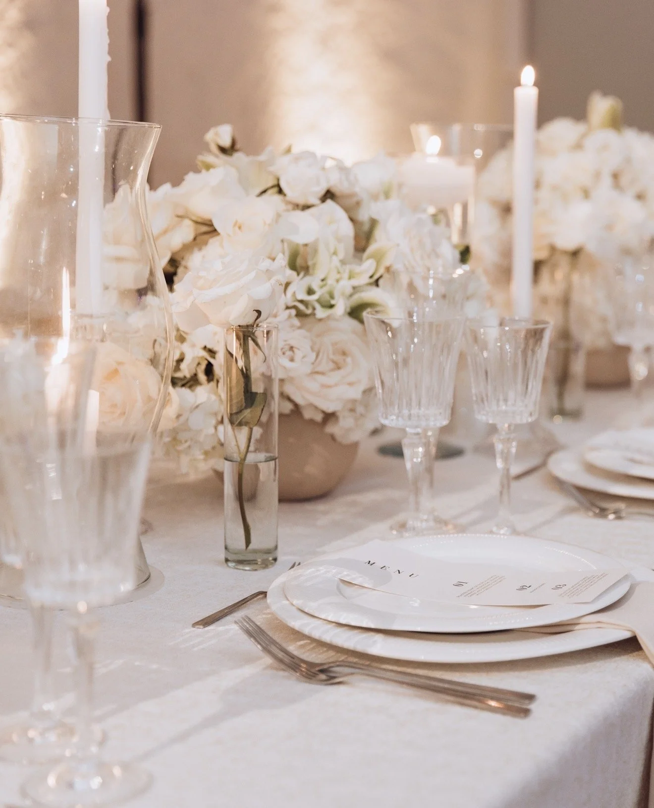 Elegant dining table with white floral centerpiece, candles, glassware, and place settings on white tablecloth