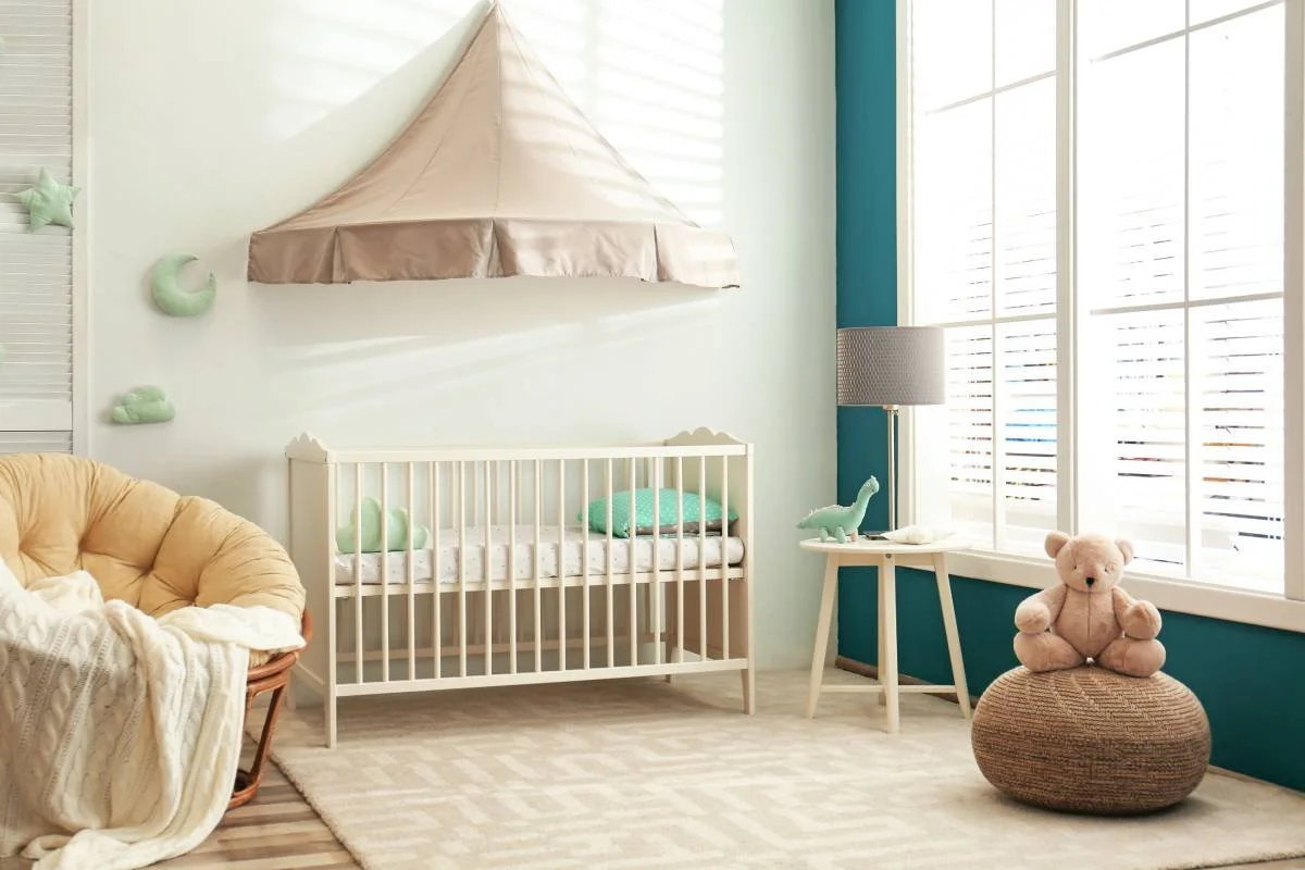 Modern nursery with teal walls and white window blinds.