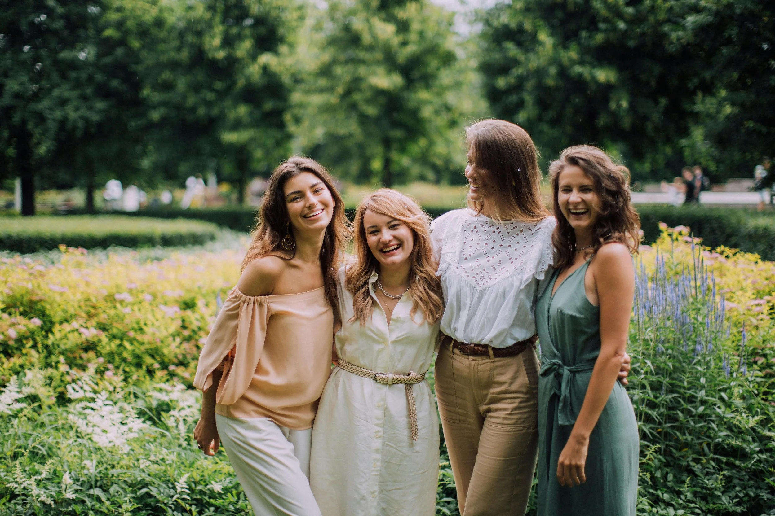 Four women standing together outdoors in a garden, smiling and posing for a photo.