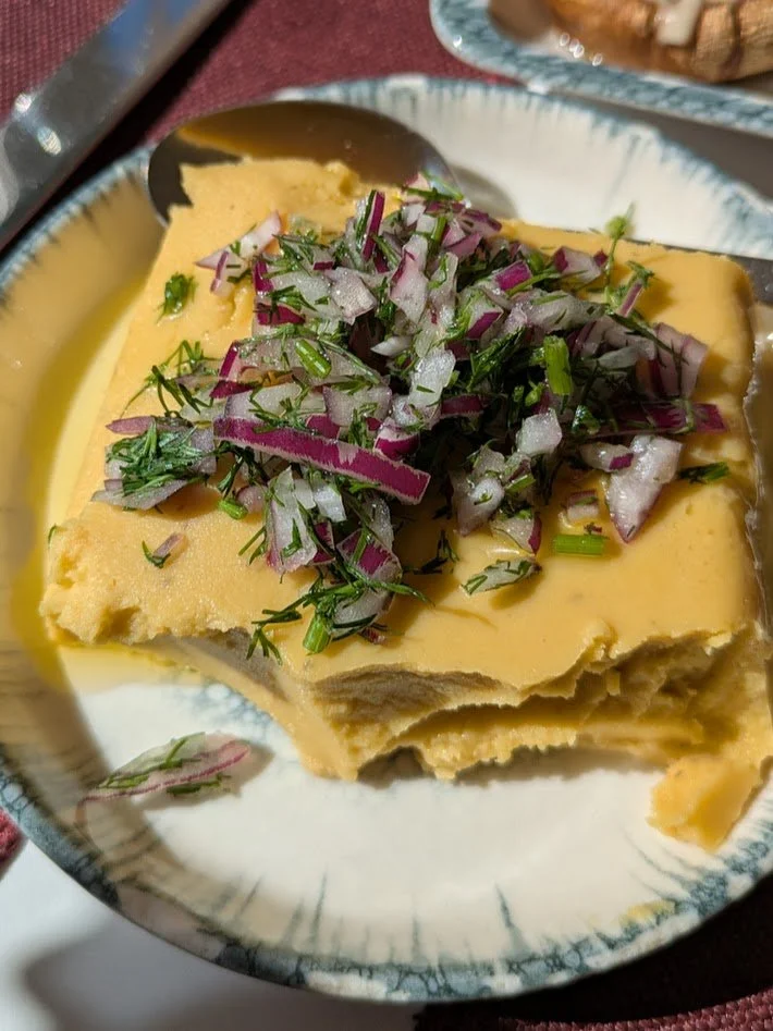 Fava - made of  fava beans which are boiled with onion olive oil and seasonings and then pureed. The resulting paste is chilled until it sets (kind of like a jello mold). It is served cold, sprinkled with olive oil, chopped parsley and red onion. The