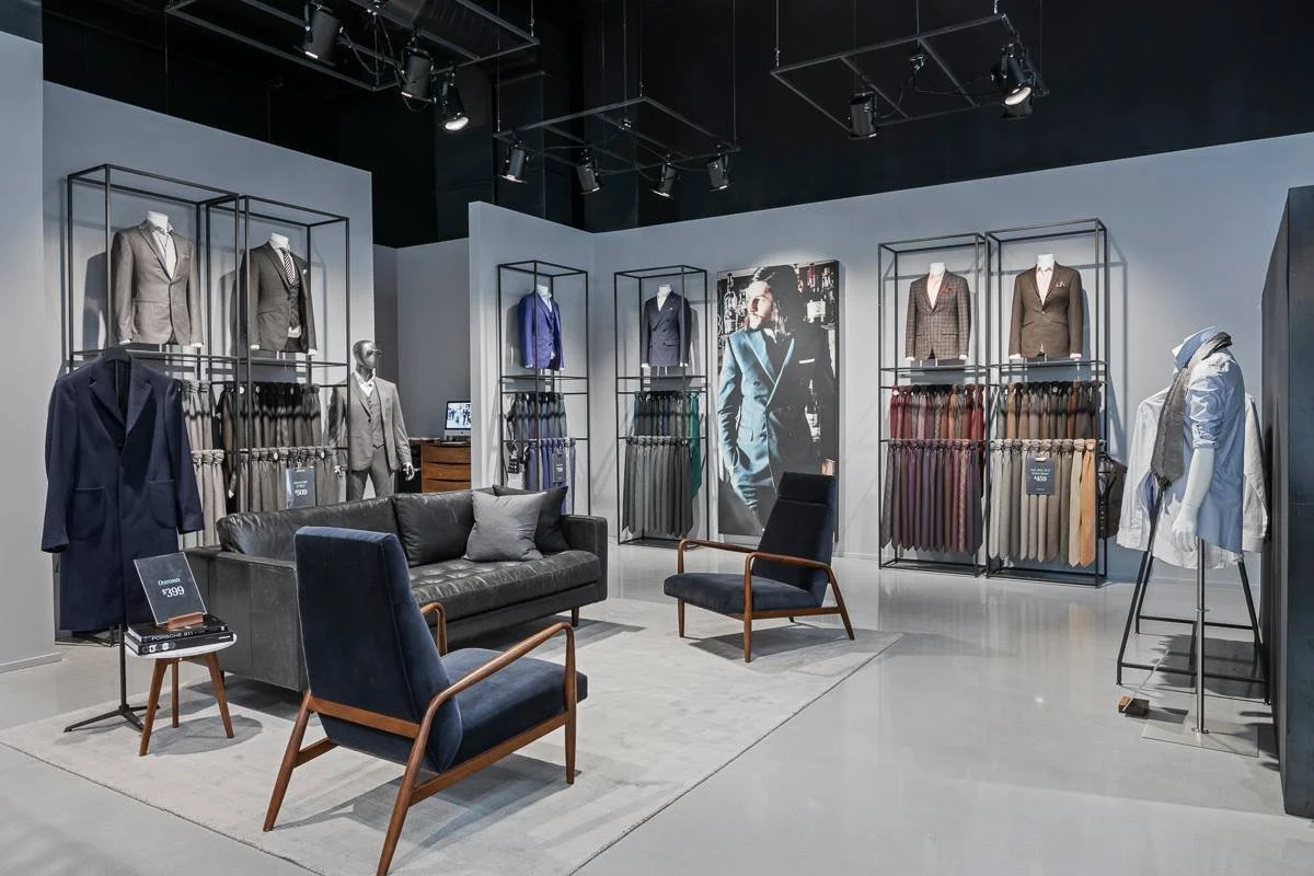 Industrial-style Indochino suit shop interior with exposed ceiling, tailored racks, and navy lounge seating