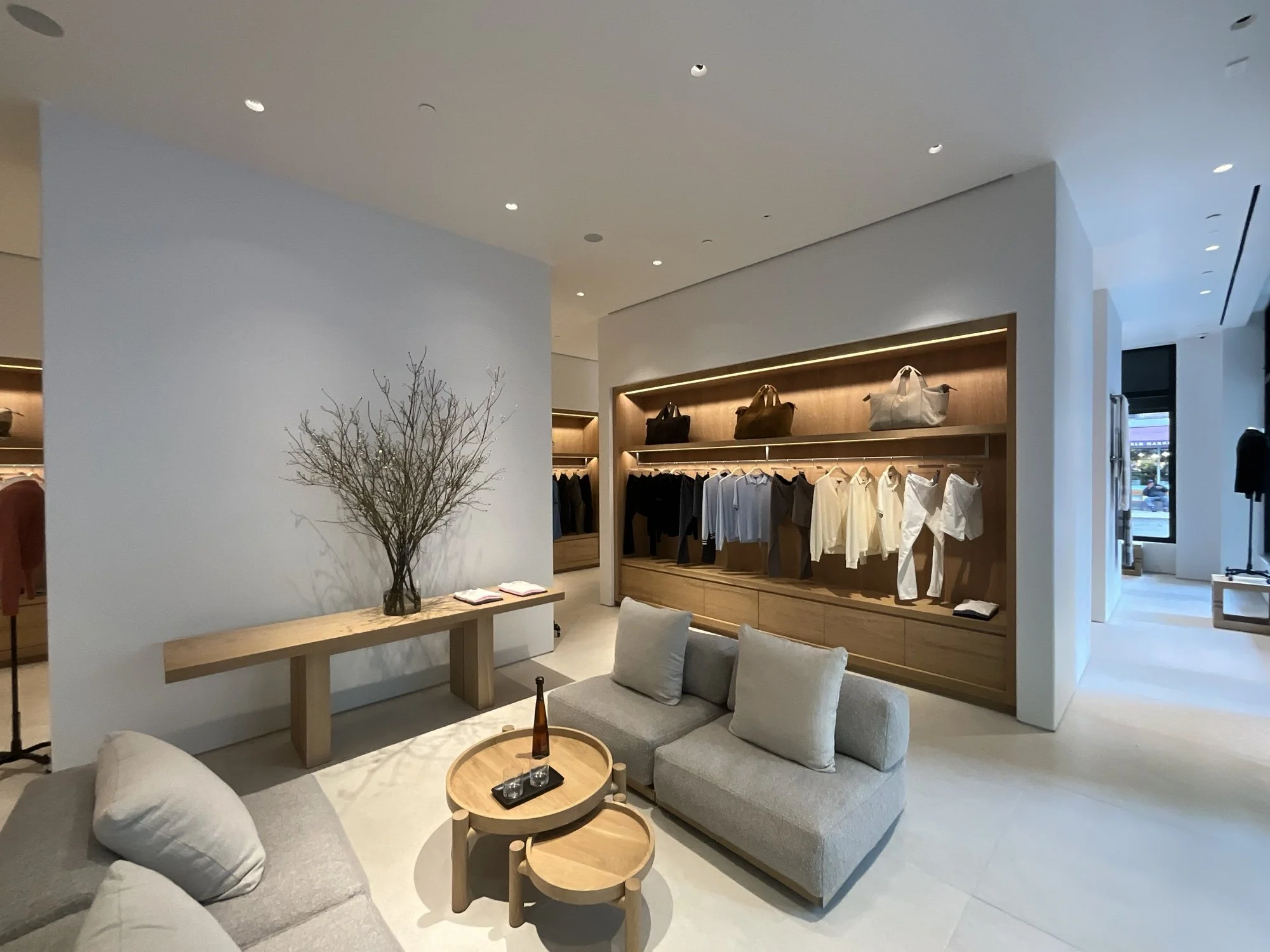 Minimalist James Perse seating area with branch centerpiece and wood-shelved apparel wall