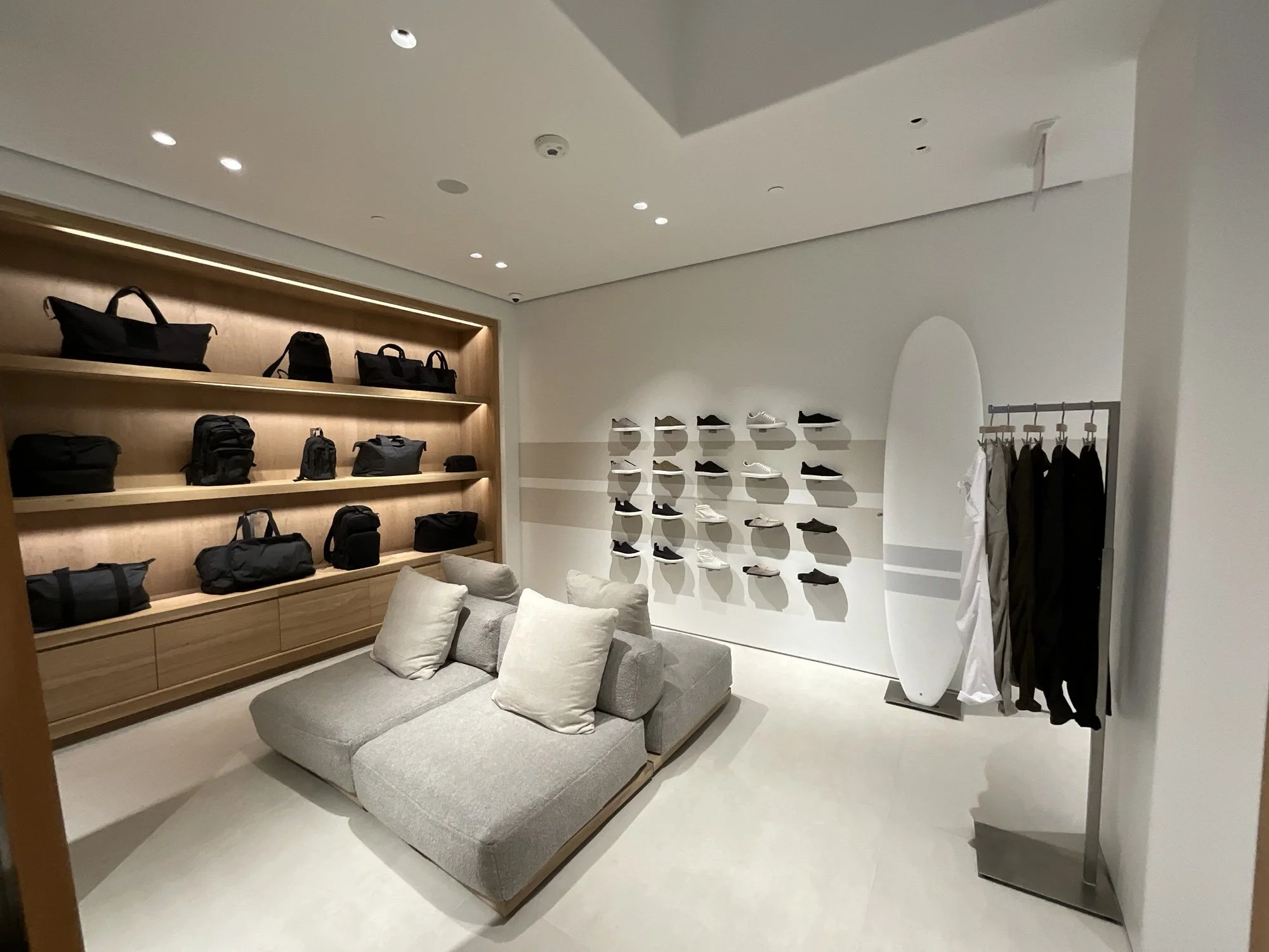 James Perse lounge nook with grey sofa, surfboard display, and wood shoe shelving