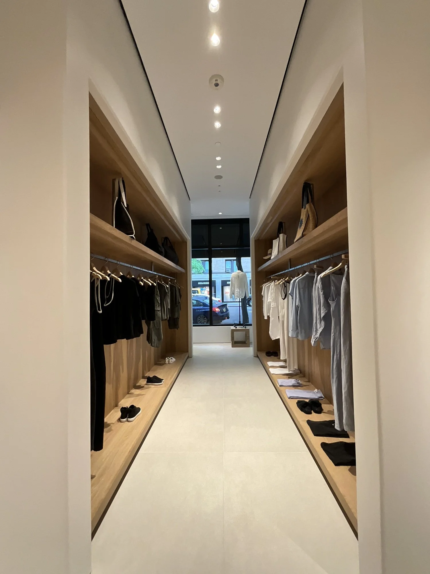 Narrow James Perse retail corridor with wood shelving and floor-to-ceiling clothing displays
