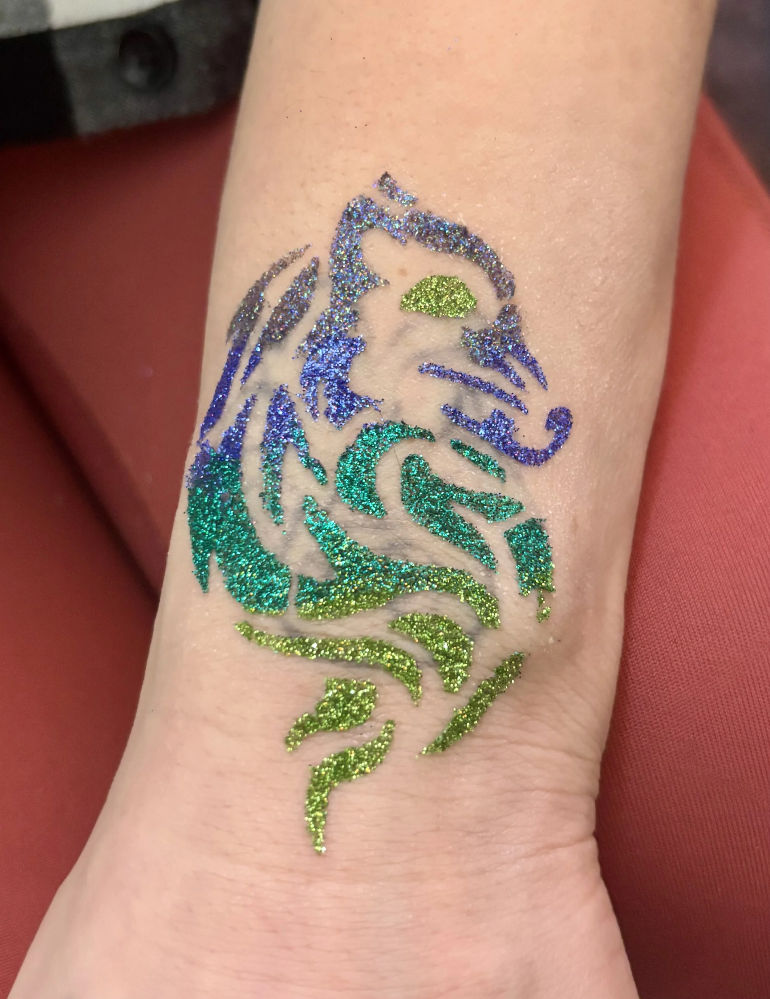 Colorful glitter tattoo of a roaring tiger with green, blue, purple, and yellow accents on a person's arm.