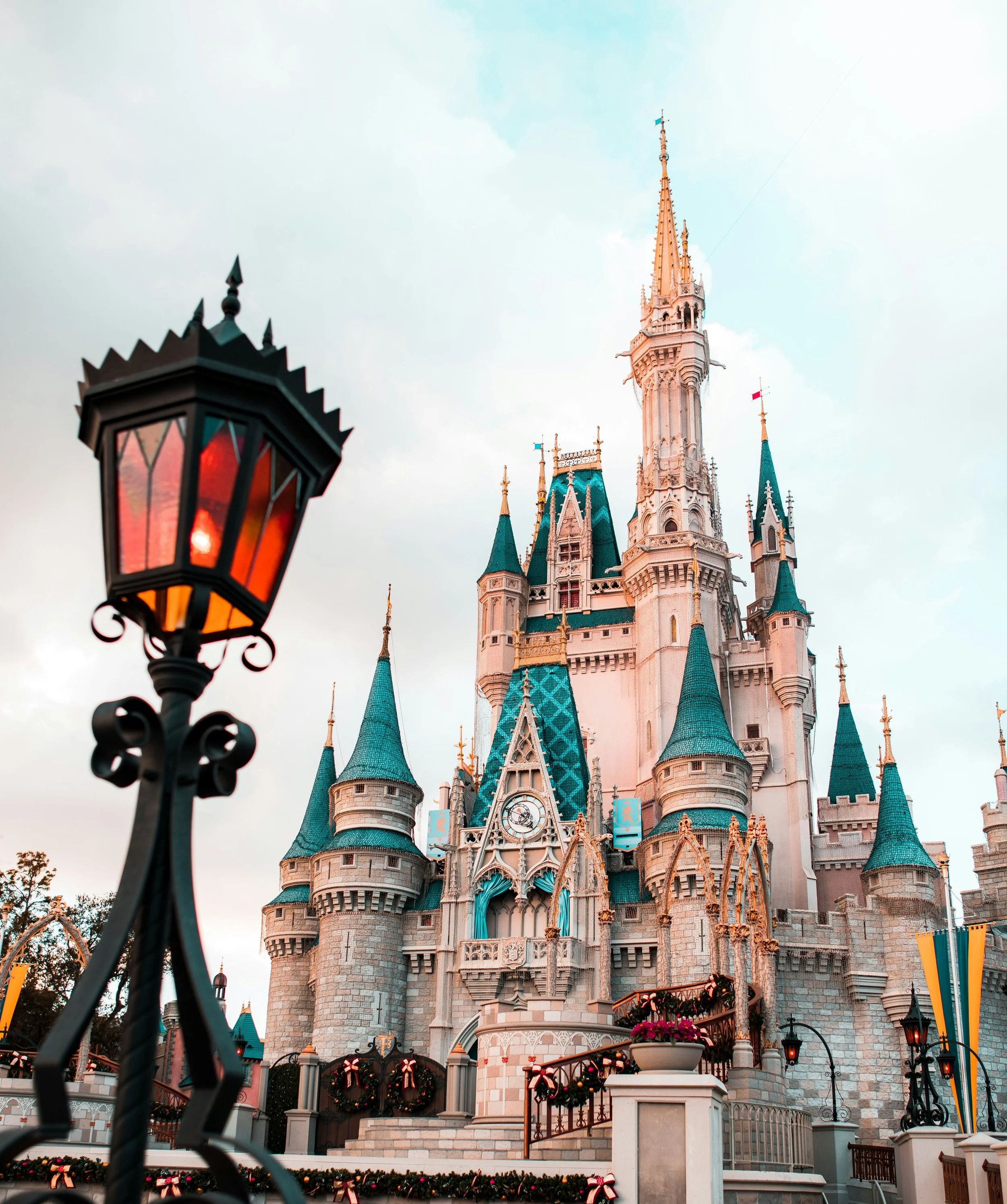 Castelo da Disney com torres azuladas decoradas e uma lâmpada de ferro à frente, durante o fim de tarde.