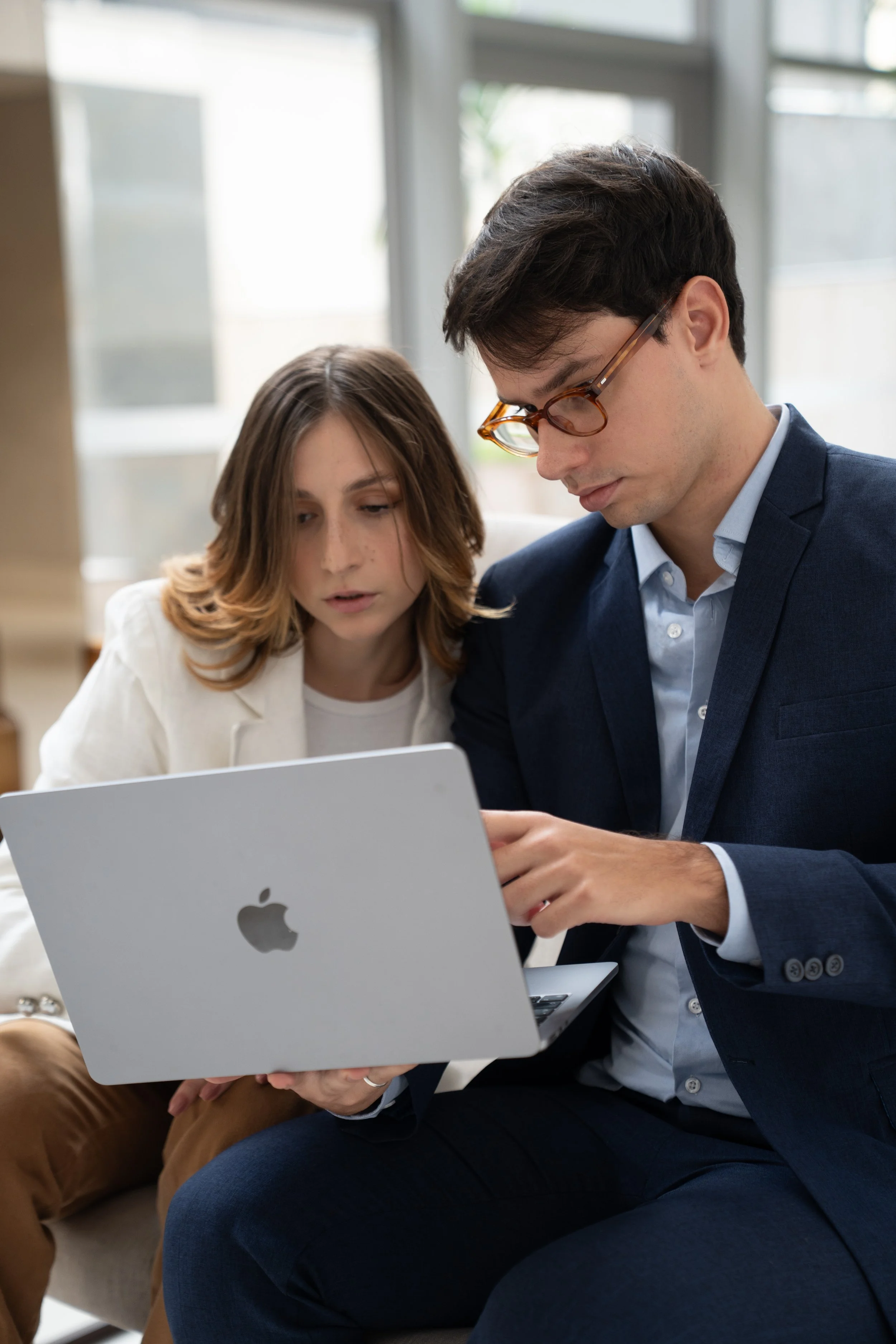 Homens e mulher olhando uma tela de laptop juntos em uma sala com janela ao fundo.