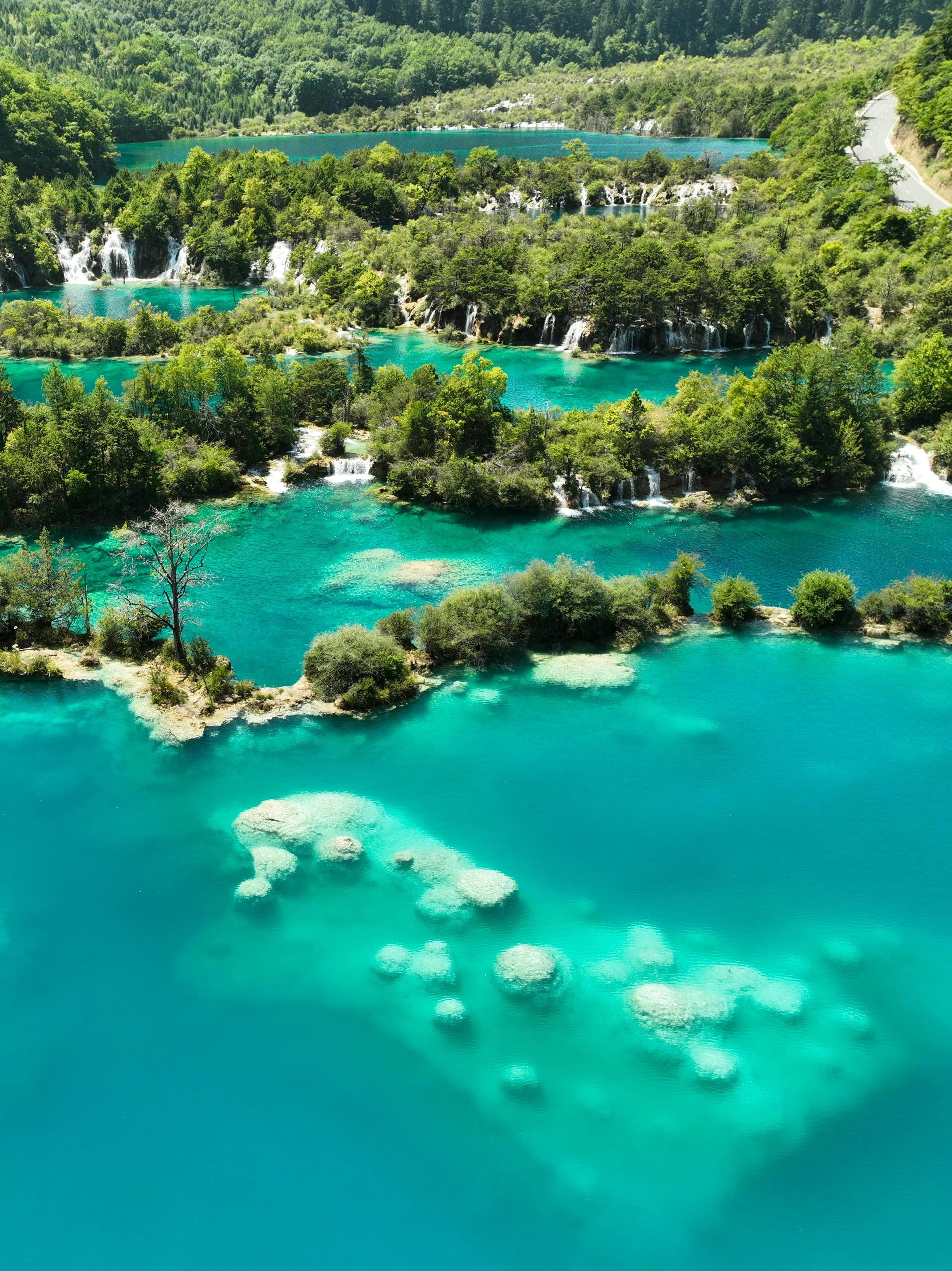 Aerial view showing tiers of turquoise lakes feature waterfalls connecting each level. Bright green trees surround the lakes