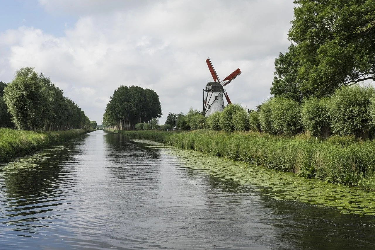 The shot looks down a beautiful treelined river, with the right of shot dominated by a white windmill with red sails