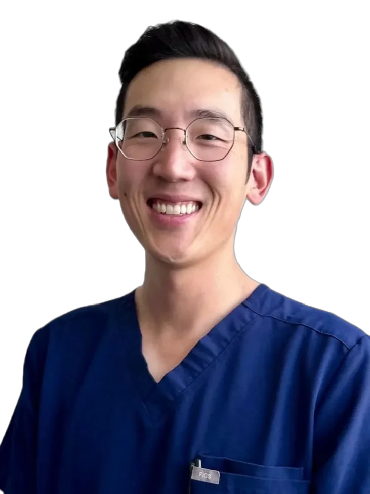 A smiling man in navy medical scrubs and glasses against a white background.