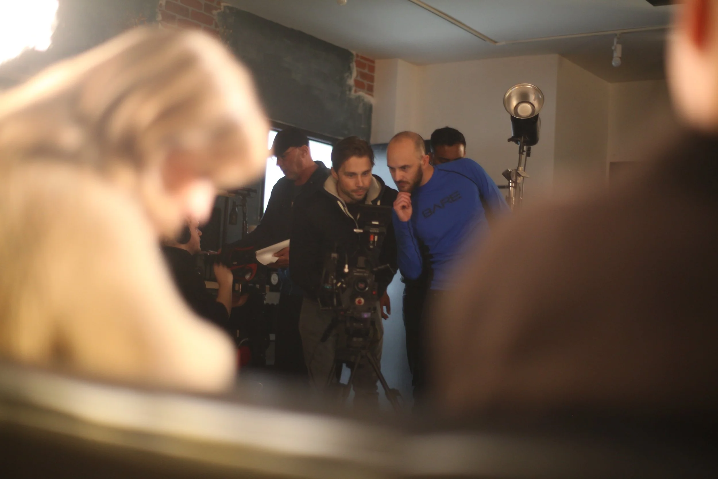 Filmmakers and crew reviewing footage on a film set, with camera and equipment visible, and blurred foreground and background.