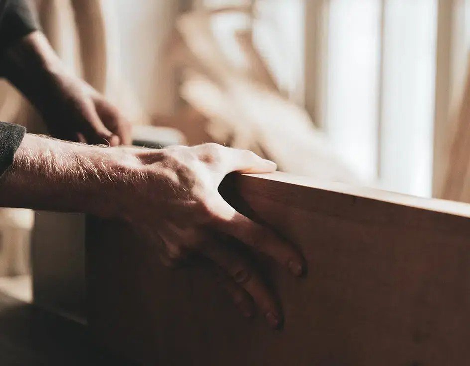 A person’s hand smoothing a piece of wood during woodworking.