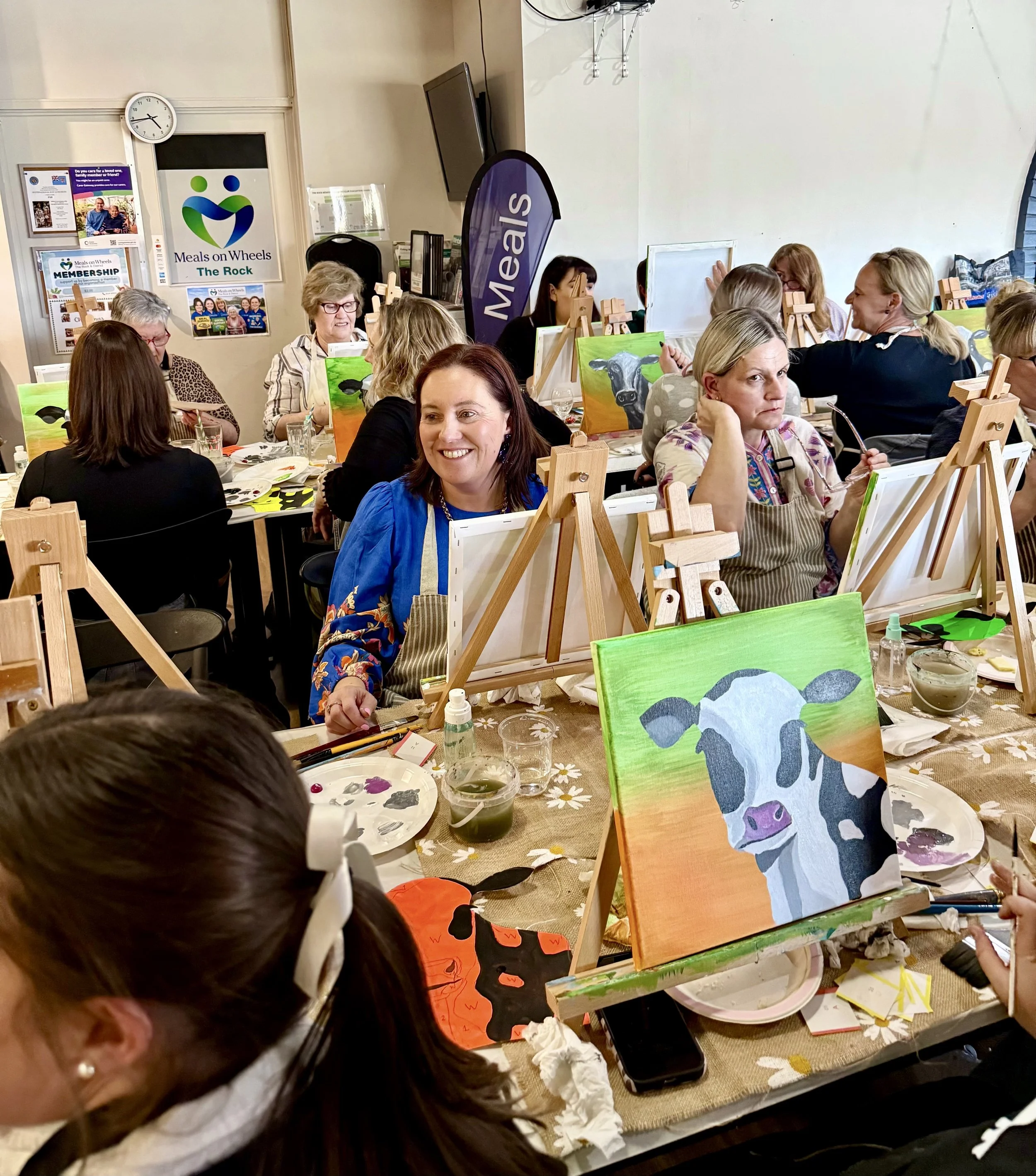 Private group event doing paintings of black and white cows with orange and green backgrounds